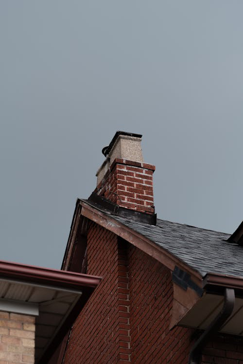 Low-angle view of a house roof with chimney against a blue sky