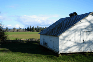a white barn in a green field with metal roofing